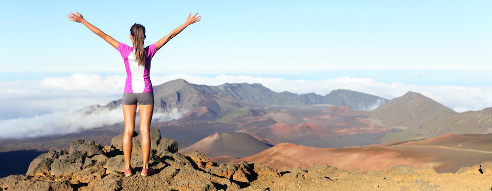 Woman standing atop a mountain with arms in the air, celebrating success